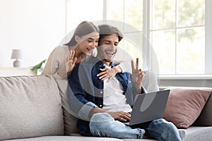 Smiling millennial european couple communicate with family remotely, wave hand, showing peace sign