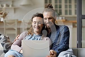 Smiling millennial family couple using computer at home.