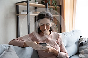 Smiling millennial girl relax on sofa using cellphone