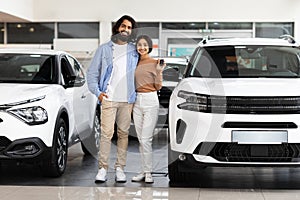 Smiling millennial indian couple standing next to new car