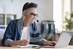 Smiling Millennial Man In Headset Watching Business Webinar At Workplace In Office