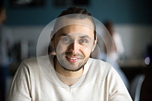 Smiling millennial man looking at camera in cafe, headshot portr