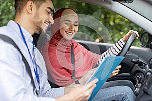 Smiling millennial middle eastern man, explain rules, put mark for driving test for woman in hijab