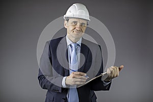 Smiling mining engineer in hard hat makes notes on clipboard and looks at camera