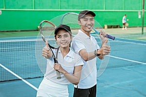 smiling mixed doubles tennis player with thumbs up holding racket