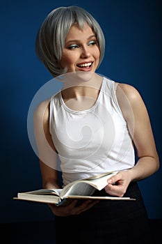 Smiling model in silver wig leafing through the book. Close up. Blue background