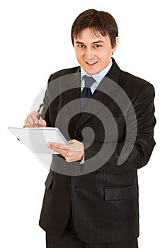 Smiling modern businessman making notes in notepad