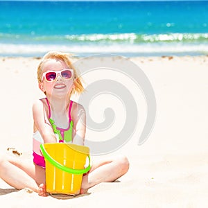 Smiling modern child on seacoast playing with yellow bucket