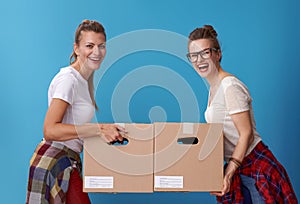 Smiling modern female roommates with cardboard boxes on blue