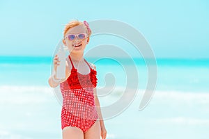 Smiling modern girl on seacoast showing suntan lotion