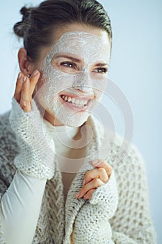 Smiling modern housewife with white facial mask touching face