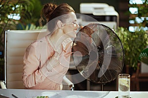 smiling modern middle aged accountant woman at work with electric fan