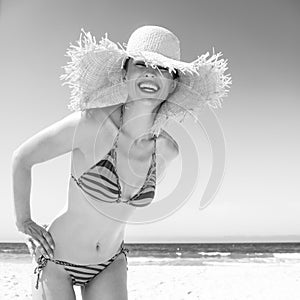 Smiling modern woman in bikini and beach straw hat on seacoast