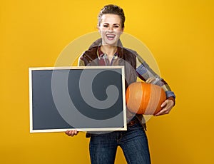 Smiling modern woman farmer with pumpkin showing blank board