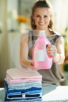 Smiling modern woman with ironing board, clothes and softener