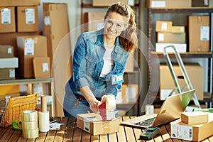 Smiling modern woman in jeans with parcels in warehouse