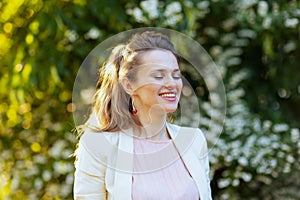 smiling modern woman in pink dress and white jacket in city