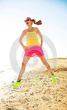 Smiling modern woman on seashore in evening jumping