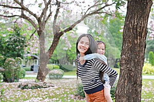 Smiling mom carrying her little child girl in garden with fully fall pink flower around. Happy loving family