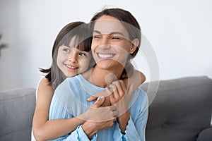 Smiling mom and cute kid daughter embracing looking into future