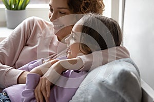 Smiling mom embracing teen daughter relaxing together at home