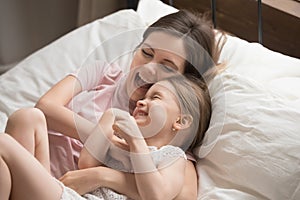 Smiling mom have fun playing with little daughter in bedroom