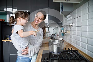 Smiling mom holding kid daughter curious about cooking in kitche