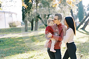 Smiling mom hugging shoulders of dad kissing little girl in his arms