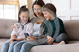 Smiling mom with kids relax at home using smartphone