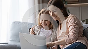 Smiling mom and little daughter using laptop at home