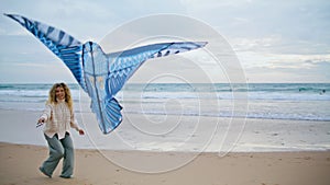 Smiling mom playing kite with child on seaside. Joyful parent launching toy