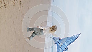 Smiling mom playing kite with child on seaside. Parent launching toy vertical