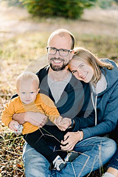 Smiling mom put her head on dad shoulder hugging him with a little boy on his lap