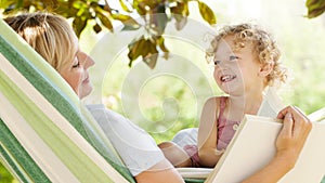 Smiling mom reading a story from the book to the little girl daughter child blue eyes with blond curly hair, together lying on the