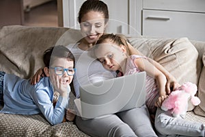 Smiling mom relaxing with kids on sofa watching cartoons