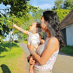 Smiling mom showing blooms of linden tree to baby boy