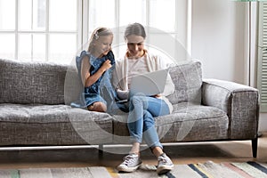 Smiling mom and small daughter use laptop at home