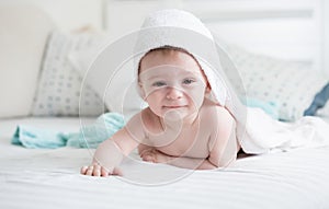 Portrait of smiling 9 months old baby boy lying on bed under white towel after washing in bath