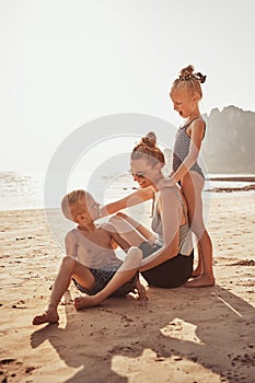 Smiling Mother and adorable children sitting on a sandy beach