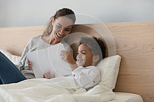 Smiling mother with African American child reading book in bed