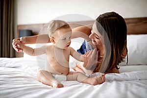 Smiling mother and baby in bed. Young mom playing with her son.