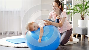 Smiling mother and baby doing fitness exercises on fitball at home. Concept of child healthcare, kids sports and yoga