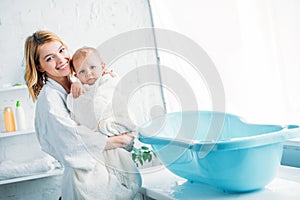 smiling mother in bathrobe carrying adorable child