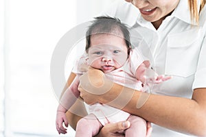 Smiling mother carrying of her newborn baby girl at home. Cute 19 days Asian Australian infant baby looking at camera, smiling.