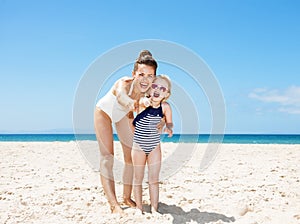 Smiling mother and child pointing in camera at sandy beach