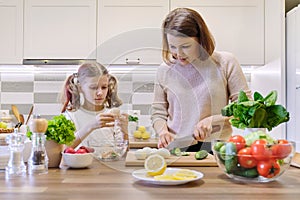 Smiling mother and daughter 8, 9 years old cooking together in kitchen vegetable salad. Healthy home food, communication parent