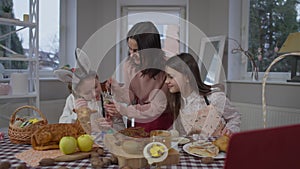 Smiling mother and daughter coloring egg on Easter sitting at table with charming teenage girl. Portrait of happy