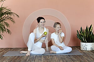 Smiling mother and daughter eating fruits after practicing yoga together