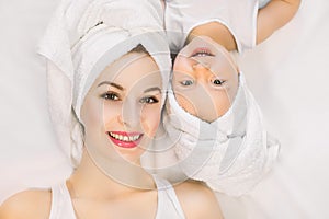 Smiling mother and daughter lying on white background, bathtime concept. Pretty young woman with little girl wearing