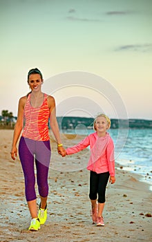 Smiling mother and daughter on seashore in evening walking